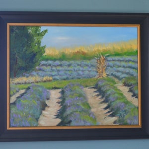 Puede incluir: Una pintura al &oacute;leo enmarcada que representa un campo de lavanda con un solo tallo alto de hierba seca en el centro. El campo est&aacute; dividido en filas por caminos de tierra. La pintura tiene un cielo azul claro y un &aacute;rbol verde en el fondo.