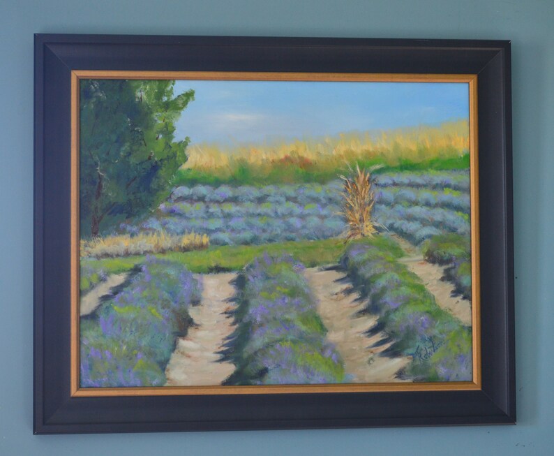 Puede incluir: Una pintura al &oacute;leo enmarcada que representa un campo de lavanda con un solo tallo alto de hierba seca en el centro. El campo est&aacute; dividido en filas por caminos de tierra. La pintura tiene un cielo azul claro y un &aacute;rbol verde en el fondo.