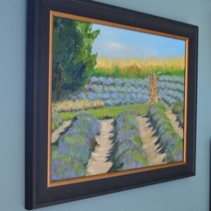 Puede incluir: Una pintura al &oacute;leo enmarcada que representa un campo de flores de lavanda. La pintura presenta un cielo azul brillante, &aacute;rboles verdes y un camino que atraviesa el campo de lavanda.