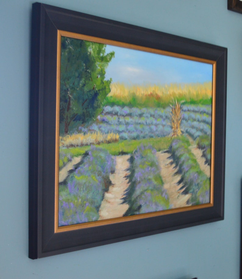 Puede incluir: Una pintura al &oacute;leo enmarcada que representa un campo de flores de lavanda. La pintura presenta un cielo azul brillante, &aacute;rboles verdes y un camino que atraviesa el campo de lavanda.