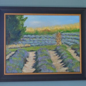 Puede incluir: Una pintura al &oacute;leo enmarcada que representa un campo de lavanda con un solo tallo alto de hierba seca en el centro. El campo est&aacute; dividido en filas por caminos de tierra. La pintura tiene un cielo azul claro y un &aacute;rbol verde en el fondo.