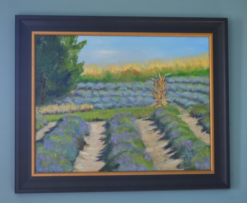 Puede incluir: Una pintura al &oacute;leo enmarcada que representa un campo de lavanda con un solo tallo alto de hierba seca en el centro. El campo est&aacute; dividido en filas por caminos de tierra. La pintura tiene un cielo azul claro y un &aacute;rbol verde en el fondo.