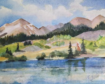 May include: A watercolor painting depicting a blue lake in the foreground with reflections of the landscape. The midground features green hills with scattered evergreen trees, while the background shows tall, light brown mountain peaks under a blue sky.