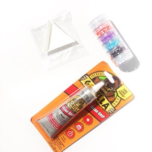 May include: An assortment of craft supplies on a white background. Includes a tube of Gorilla Clear Grip contact adhesive, a stack of glitter containers in various colors, and a white triangular tray.