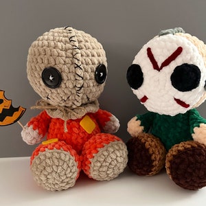 Puede incluir: Dos peluches de crochet con tem&aacute;tica de Halloween. Uno es un personaje inspirado en Michael Myers, de color marr&oacute;n y naranja, con una calabaza. El otro es un personaje inspirado en Jason Voorhees, de color blanco y verde, con una m&aacute;scara de hockey.