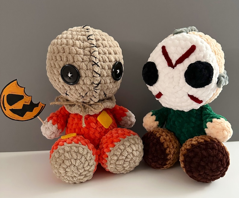 Puede incluir: Dos peluches de crochet con tem&aacute;tica de Halloween. Uno es un personaje inspirado en Michael Myers, de color marr&oacute;n y naranja, con una calabaza. El otro es un personaje inspirado en Jason Voorhees, de color blanco y verde, con una m&aacute;scara de hockey.