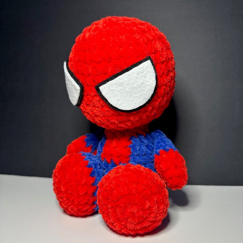 Peut inclure: Un jouet en peluche en crochet rouge et bleu en forme de Spiderman. Le jouet a des yeux en feutre blanc avec un contour noir.