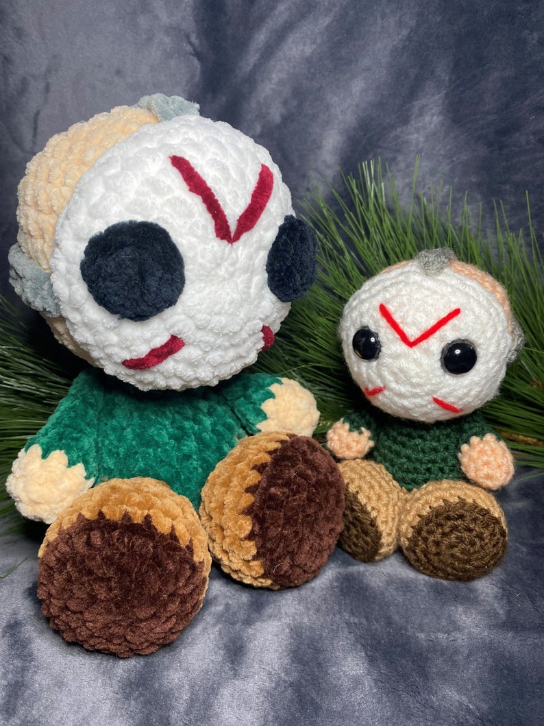 Puede incluir: Dos peluches de crochet de un personaje de pel&iacute;cula de terror. El peluche m&aacute;s grande es verde y blanco con una raya roja en la cara. El peluche m&aacute;s peque&ntilde;o es verde y blanco con una raya roja en la cara. Ambos peluches tienen ojos negros.