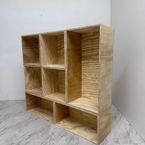 May include: A wooden shelf unit with six open compartments. The shelf is made of unfinished plywood and has a natural wood grain.