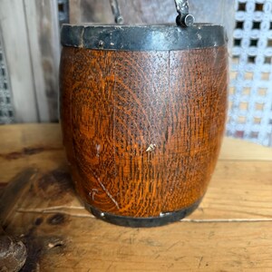 May include: A small, wooden barrel with a metal rim and handle. The barrel has a dark brown, aged appearance with visible wood grain. The metal rim and handle are silver and black. The barrel is likely a decorative item or small container.