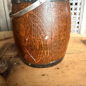May include: A vintage wooden bucket with a metal rim and handle. The bucket has a rich, warm brown color with visible wood grain. The metal rim and handle are silver-toned, adding a touch of contrast to the rustic design.