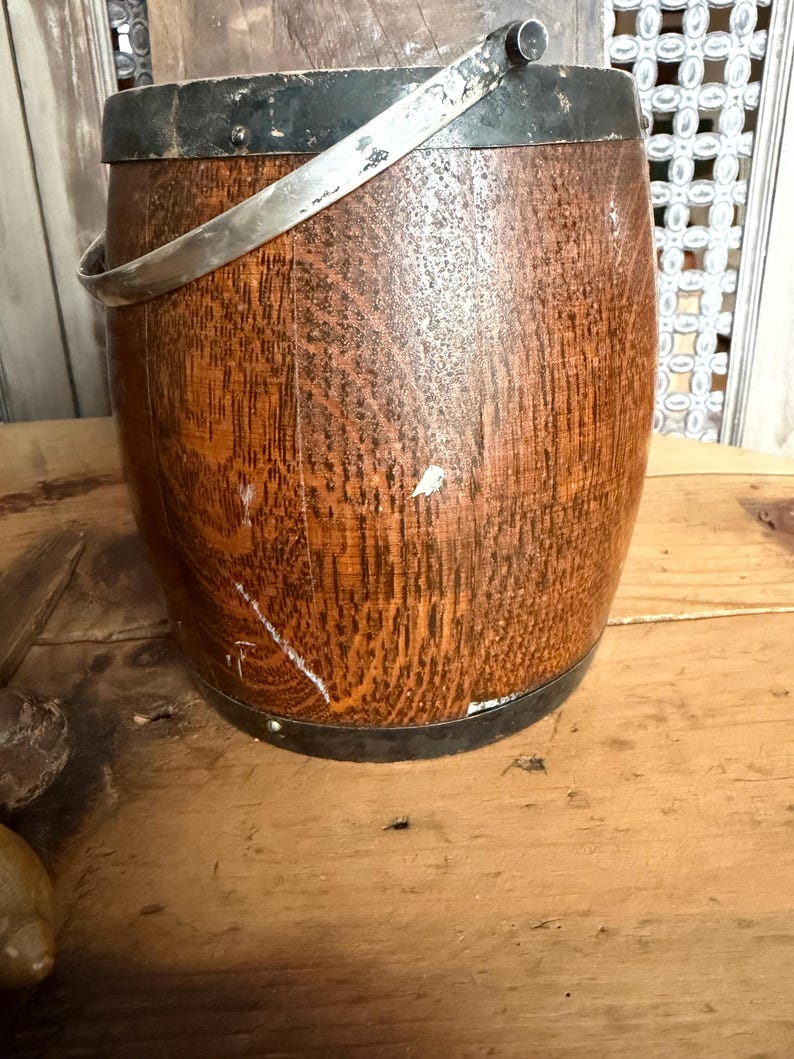 May include: A vintage wooden bucket with a metal rim and handle. The bucket has a rich, warm brown color with visible wood grain. The metal rim and handle are silver-toned, adding a touch of contrast to the rustic design.