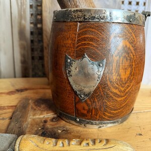 May include: A wooden ice bucket with a silver rim and a shield-shaped emblem. The bucket has a wooden pestle inside. A wooden-handled knife with the word "GENTLEMAN" is in the foreground. The items are on a wooden surface.