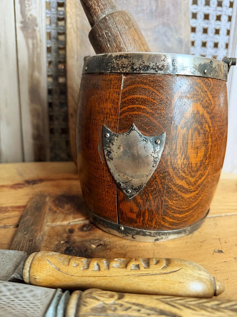 May include: A wooden ice bucket with a silver rim and a shield-shaped emblem. The bucket has a wooden pestle inside. A wooden-handled knife with the word "GENTLEMAN" is in the foreground. The items are on a wooden surface.