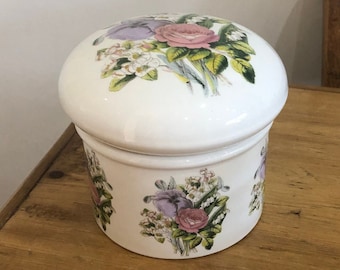 May include: White ceramic jar with a floral design. The lid and jar are decorated with a bouquet of pink, purple, and white flowers with green leaves.