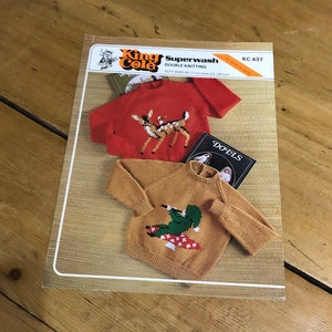 May include: A vintage knitting pattern book featuring two knitted sweaters. One is red with a deer design, and the other is tan with a green alligator design. The book is labeled "King Cole Superwash Double Knitting" and includes sizing information.