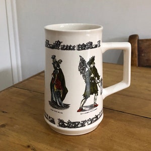 May include: White ceramic mug with a handle. The mug has a black and white illustration of people in historical clothing. The text "Come with me Sir" and "Buy a Rabbit, Buy a Rabbit" is printed on the mug.