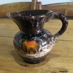 May include: A brown ceramic pitcher with a white and orange glaze. The pitcher has a wide mouth and a handle.