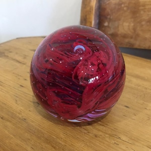 Può includere: Un fermacarte di vetro rosso con vortici bianchi e viola e bolle d'aria.