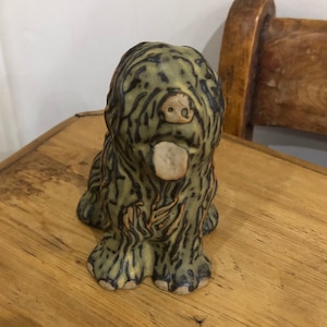 May include: A ceramic dog figurine with a green and brown glaze. The dog is sitting with its tongue sticking out.