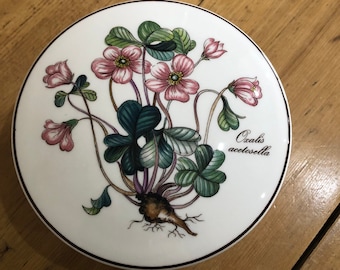 May include: A white ceramic trinket box with a floral design featuring pink flowers and green leaves. The text "Oxalis acetosella" is printed on the box.