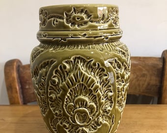 Puede incluir: Un jarrón de cerámica verde con un intrincado diseño floral en relieve. El jarrón tiene un cuerpo redondeado y una boca ancha.