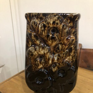 May include: A brown and black ceramic vase with a floral design. The vase has a rectangular shape and a wide opening.