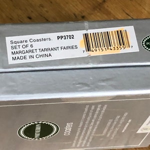 May include: A silver box with a white label that reads "Square Coasters. PP3702 SET OF 6 MARGARET TARRANT FAIRIES MADE IN CHINA" and a barcode. The box is on a wooden surface.