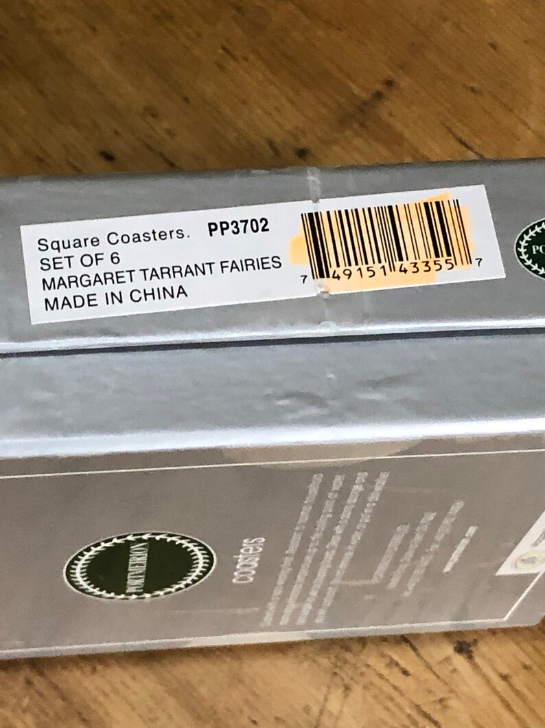 May include: A silver box with a white label that reads "Square Coasters. PP3702 SET OF 6 MARGARET TARRANT FAIRIES MADE IN CHINA" and a barcode. The box is on a wooden surface.