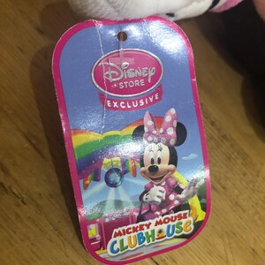 May include: Pink Minnie Mouse plush toy with a Disney Store Exclusive tag. The tag features a rainbow background with Minnie Mouse in a pink and white polka dot dress. The tag also says "Mickey Mouse Clubhouse".