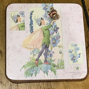 May include: A pink and white coaster with a fairy illustration. The fairy is wearing a green dress and has wings. The fairy is holding a butterfly with black and orange wings. The coaster has a floral design and the text "The Medici Society Limited, London NW9 6JZ" in the bottom right corner.