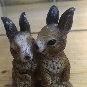 May include: Two brown and white ceramic rabbit figurines standing side by side. The rabbits have black ears and brown fur with white markings.