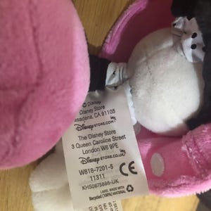 May include: Pink and black plush toy with a white tag attached. The tag has the Disney Store logo and information about the store's location and website. The tag also includes the product number, W818-7201-5, and the CE mark.