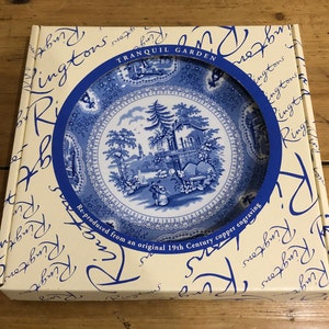 Op de afbeelding: Een witte doos met blauwe rand met daarop een blauw en wit keramiek bord met een bloemenmotief. De doos heeft de tekst "Tranquil Garden" en "Re-produced from an original 19th Century copper engraving".
