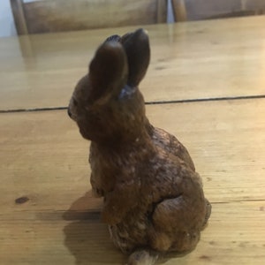 May include: A brown ceramic rabbit figurine with a detailed textured surface. The rabbit is sitting upright with its ears perked up.