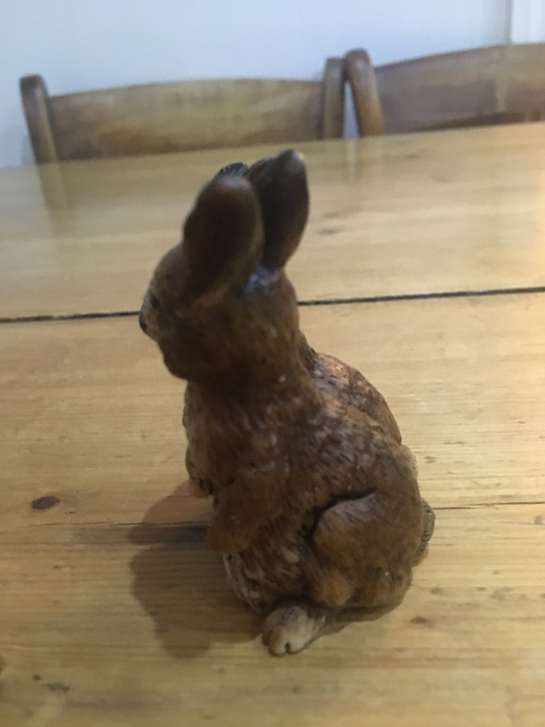 May include: A brown ceramic rabbit figurine with a detailed textured surface. The rabbit is sitting upright with its ears perked up.