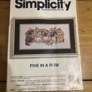 Op de afbeelding: Simplicity kruissteekpakket met een ingelijst ontwerp van vijf kittens tussen rozen. De set bevat een getekend ontwerp, een naald en instructies. Afmeting: 41 cm x 20 cm.