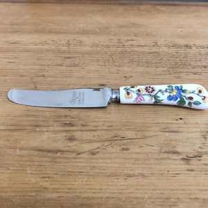 May include: A butter knife with a stainless steel blade and a white handle decorated with colorful floral patterns. The handle features blue, yellow, pink, and red flowers. The blade has text that reads "Coalport England".