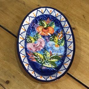May include: An oval ceramic serving dish with a blue background and a white border. The dish is decorated with a floral design in shades of pink, orange, yellow, and blue.