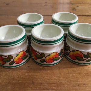 May include: Set of five white ceramic egg cups with green and red apple designs.