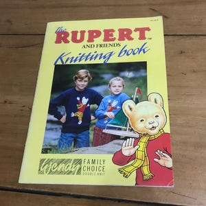 Può includere: Un libro di maglia giallo intitolato "The Rupert and Friends Knitting book". La copertina presenta un orso dei cartoni animati e due bambini con maglioni. È visibile anche il testo "Wendy Family Choice Double Knit".