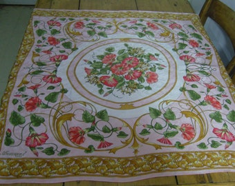 May include: A pink silk scarf with a floral pattern of pink and white morning glories. The scarf has a gold border with a repeating pattern of stylized leaves and vines. The scarf is signed "Mancini" in the lower left corner.