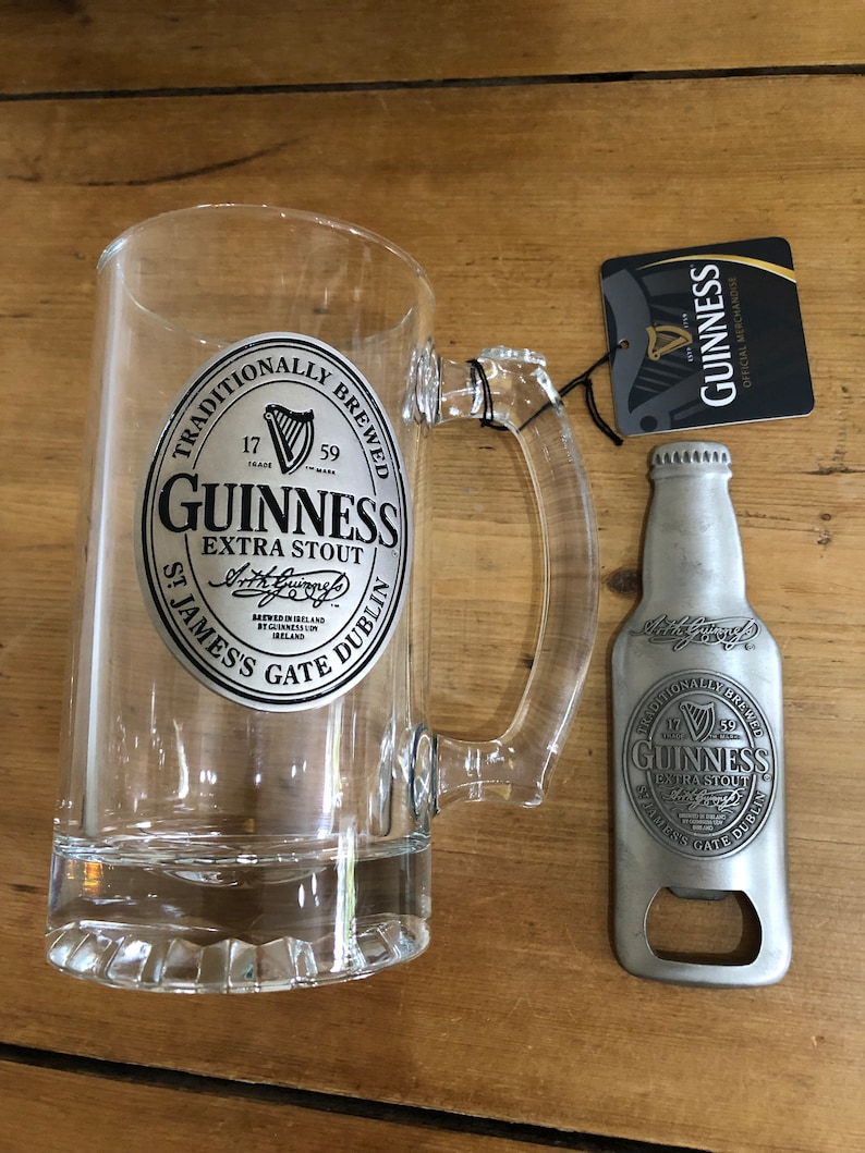 May include: A clear glass beer mug with a silver Guinness logo and a silver bottle opener with a Guinness logo. The bottle opener is shaped like a beer bottle.