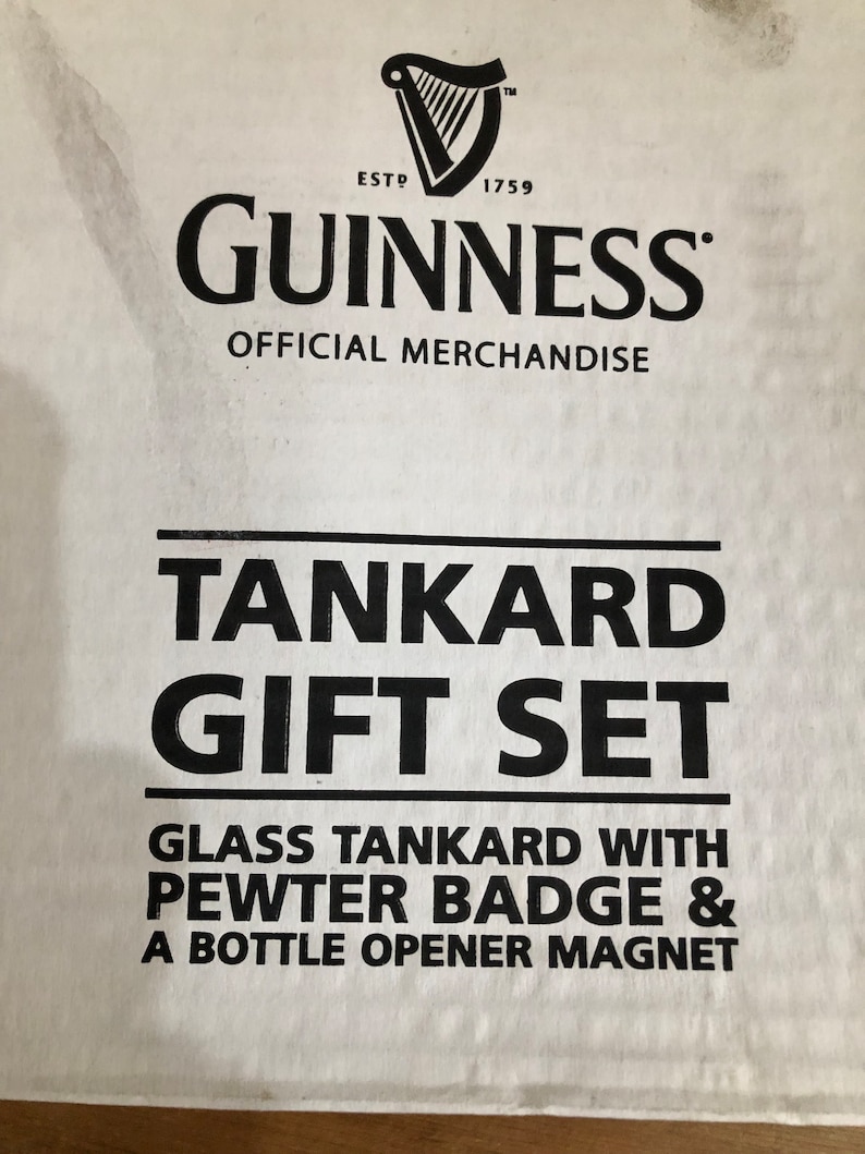 May include: A white box with black text that reads "GUINNESS OFFICIAL MERCHANDISE TANKARD GIFT SET GLASS TANKARD WITH PEWTER BADGE & A BOTTLE OPENER MAGNET". The Guinness logo is in the top left corner.