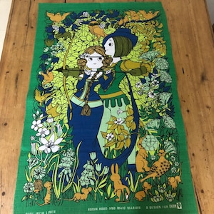 May include: Green linen tea towel with a vibrant illustration of Robin Hood and Maid Marian. The design incorporates figures, animals, and floral motifs in blue, yellow, and white. Text at the bottom reads "Pure Irish Linen" and "Robin Hood and Maid Marian".