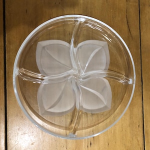 Puede incluir: Un plato de servir de vidrio transparente con un diseño de flores. El plato está dividido en cuatro secciones.