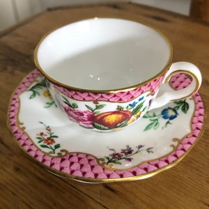 Op de afbeelding: Een witte kop en schotel set met roze en gouden details. De kop en schotel hebben een bloemenpatroon met een perzikmotief. De randen zijn goudkleurig.