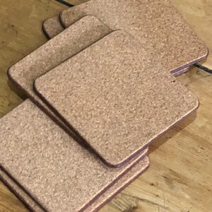 May include: A set of six brown cork coasters with a slightly textured surface. The coasters are square shaped and have a dark brown border.