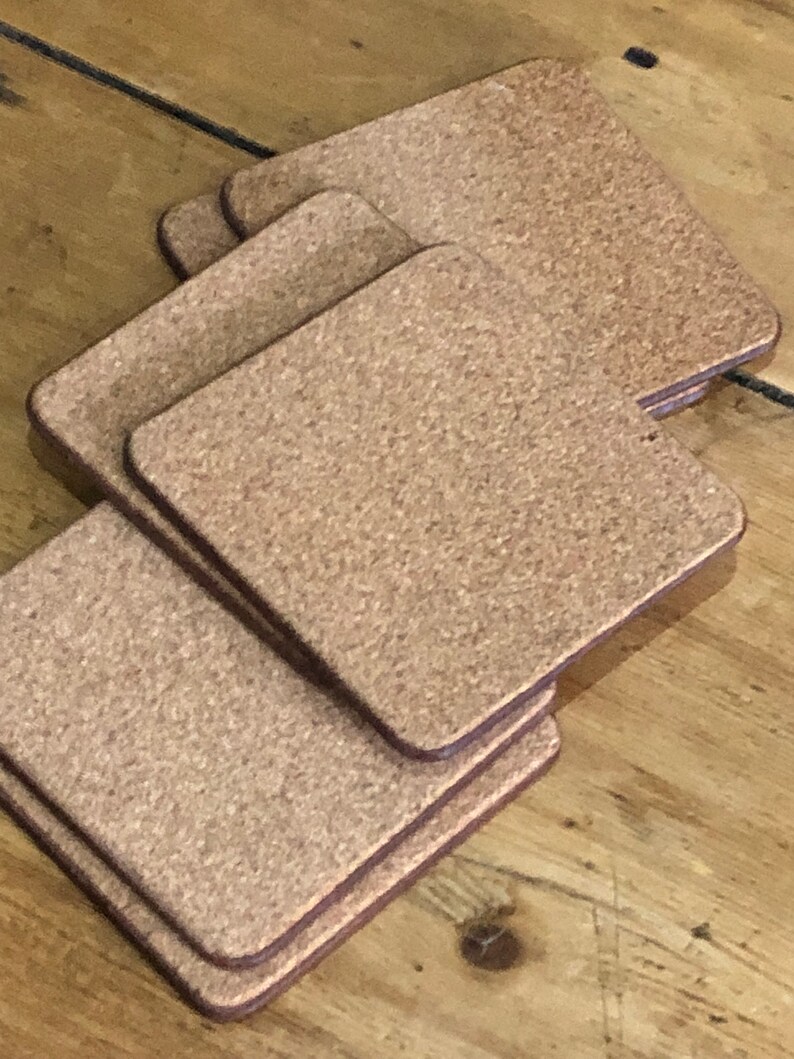 May include: A set of six brown cork coasters with a slightly textured surface. The coasters are square shaped and have a dark brown border.
