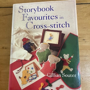 May include: A book titled "Storybook Favourites in Cross-stitch" with various cross-stitch designs. The cover displays a white sweatshirt with a cross-stitched design, framed cross-stitch, and fabric cutouts. The author's name, Gillian Souter, is also visible.
